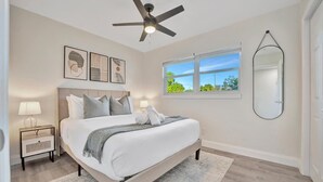 Une chambre à coucher comprenant un lit, des tables de chevet, un ventilateur de plafond, une fenêtre avec vue et un miroir fixé au mur.
