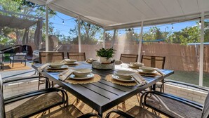 Un espace extérieur aménagé pour les repas, avec un patio couvert, un barbecue et une vue sur le jardin.