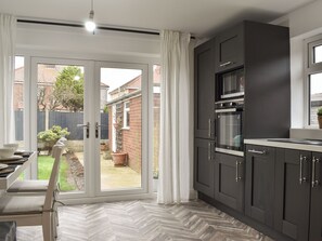 A modern kitchen with dark cabinetry, a built-in oven, and a sliding glass door leading to a garden.