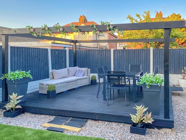 Un patio techado con sofá, mesa de comedor, sillas y plantas en macetas.