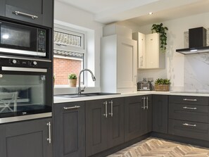 A modern kitchen with dark cabinets, a built-in oven, a sink, and a window with potted plants. - 3 bedroom accommodation in Thornton-Cleveleys, near Blackpool (Thornton-Cleveleys, near Blackpool)