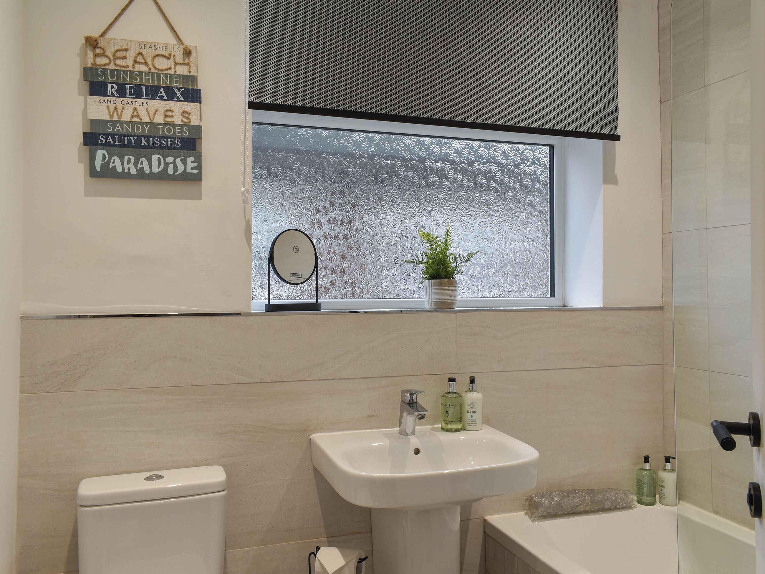 A bathroom with a toilet, sink, and bathtub. There is a window with frosted glass and a plant on the windowsill.