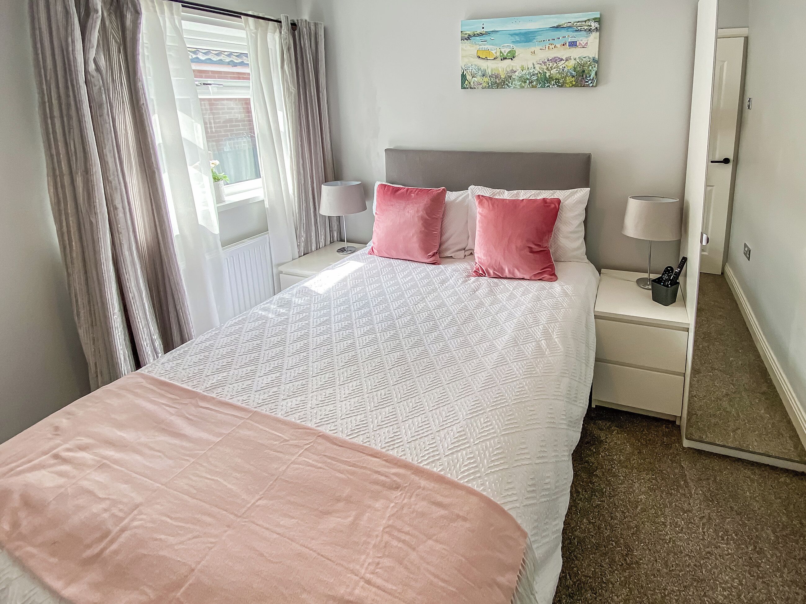 Een slaapkamer met een bed, twee nachtkastjes, een lamp, een spiegel en een raam met gordijnen.