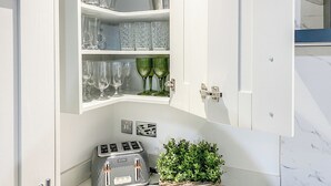 A kitchen with a Breville toaster, a cabinet with glassware, and a wicker basket with greenery.