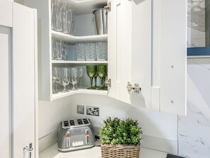 A kitchen with a Breville toaster, a cabinet with glassware, and a wicker basket with greenery.