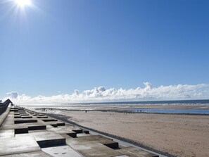 Ein Strand mit einem Betonweg, der zum Ufer führt, bewölkter Himmel und dem Meer im Hintergrund.