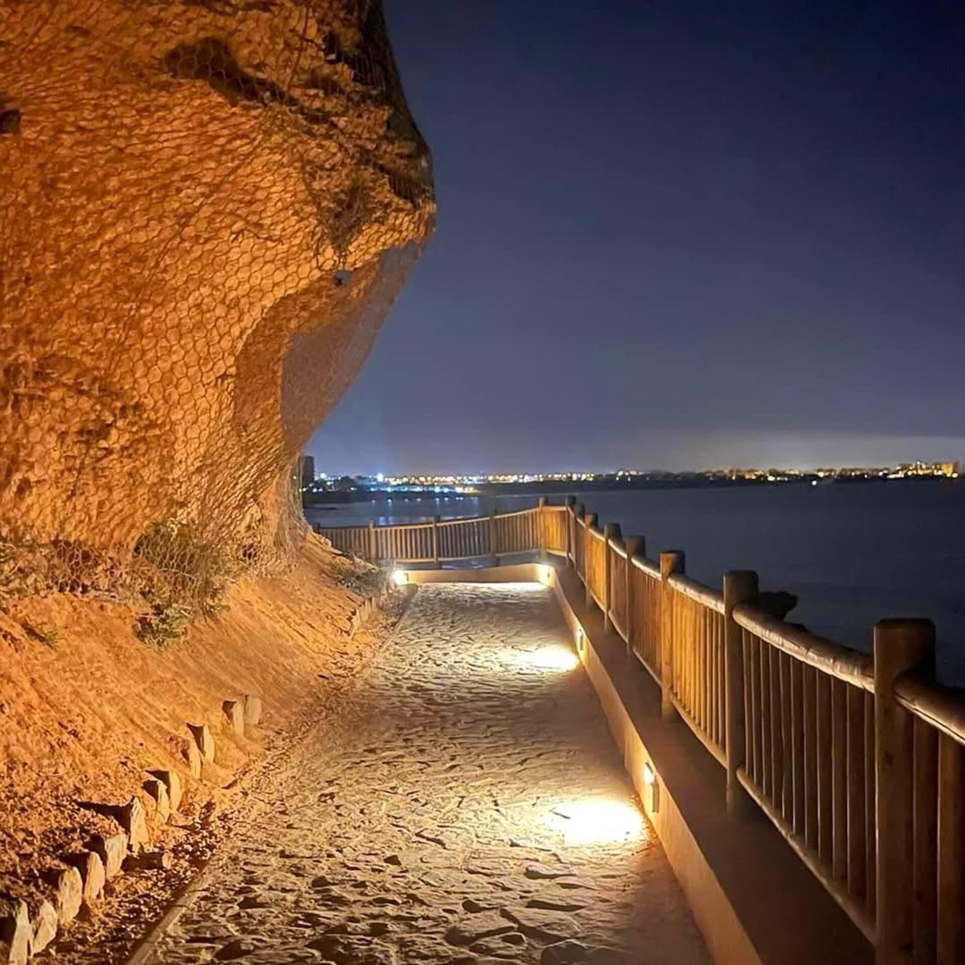 Une promenade côtière nocturne, dotée d’une rambarde en bois, qui mène à un plan d’eau.
