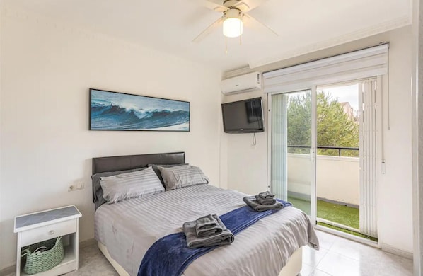 A bedroom with a bed, a television, a ceiling fan, a painting, and a balcony with a view. - Orihuela Costa, Sleeps 6 With Roof Terrace & Pool (Orihuela)