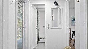 A hallway with a white door leading to a bathroom, a small table with a chair, and a hat on the floor. - Awesome apartment in Nexø with WiFi (Nexø)