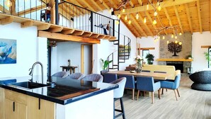 A modern kitchen with a black countertop, wooden cabinets, and a built-in sink. There is a dining area with blue chairs and a wooden table. A spiral staircase leads to an upper level with a wooden railing. - Charming Chalet in Tapalpa, Mexico with Game Lounge & Pet-Friendly Amenities! (Tapalpa)
