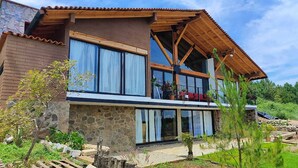 A two-story house with a stone facade, large windows, and a wooden balcony. - Charming Chalet in Tapalpa, Mexico with Game Lounge & Pet-Friendly Amenities! (Tapalpa)