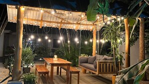 An outdoor patio area with a wooden table and benches, a sofa, and string lights.
