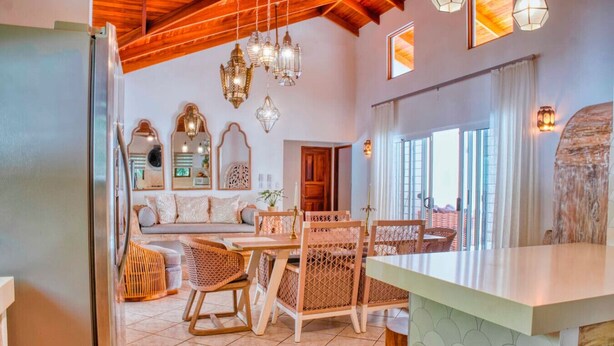 A dining area with wicker chairs, a wooden table, and hanging lanterns.