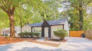 A single-story house with a dark roof, a front porch, and a driveway leading to a garage. - Charming 3-bedroom house in fabulous East Point with AC, WiFi (East Point)