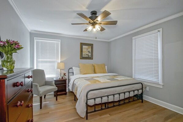 A bedroom with a bed, a chair, a dresser, a nightstand, a ceiling fan, and a window with blinds.