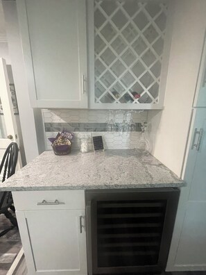 A kitchen with white cabinets, a granite countertop, and a built-in wine cooler.