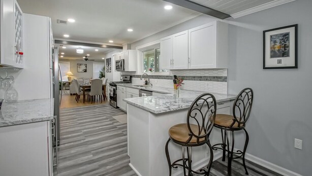 A modern kitchen with white cabinetry, a marble island, and two bar stools. - IT’S FOOTBALL TIME AT THE HIDDEN TIGER! (Baton Rouge)