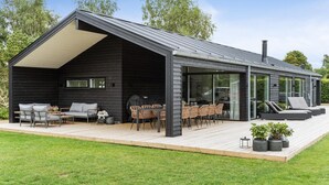 Een moderne cabin met een overdekt terras, buitenzitplaatsen en een grote schuifdeur naar de binnenruimte.
