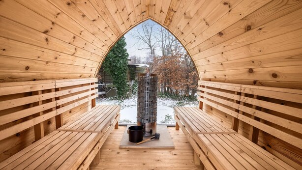 Een houten sauna met banken en sauna stenen zichtbaar door een spitsboogvenster.