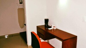 Een kleine kantoorruimte met een bureau, stoel en een wandplank met een fles en een doos.