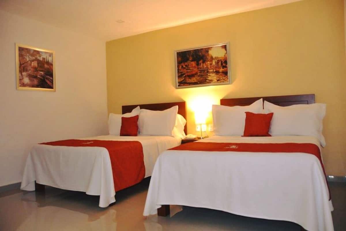 A hotel room with two beds, each with white bedding and red accents, and a painting on the wall.