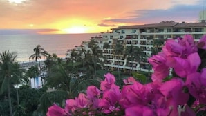 A coastal hotel with multiple balconies overlooking the sea, surrounded by lush greenery and vibrant pink flowers. - Regal 3bd PH with private pool in Beach Resort Spa (Marina Vallarta, Puerto Vallarta)