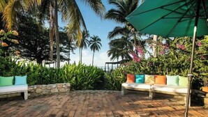 A patio with brick flooring, two white sofas with colorful cushions, and a green umbrella.