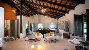 A dining area with a high ceiling, exposed beams, and a central island with a sink.