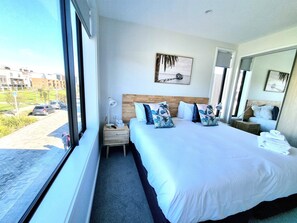 Habitación de hotel con una cama grande, una mesita de noche, una ventana con vistas a la calle y un cuadro en la pared.