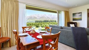 Un comedor con una mesa preparada para cuatro personas, un sofá y un amplio ventanal con vistas a la montaña.