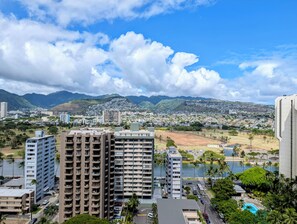 A high-rise hotel with multiple floors, a swimming pool, and a view of a cityscape with mountains in the background. - 22nd Fl, Free parking, AC, WIFI, Beautiful Mountain View (Honolulu)