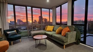 Un salon moderne doté d’une grande fenêtre offrant une vue sur le paysage urbain au coucher du soleil.