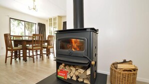 A modern living room with a wood-burning stove, a dining table with chairs, and a large window. - Narrows Hideaway-Rural retreat near Hamilton Airport (Christchurch)