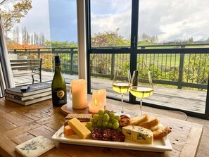 A table with a cheese platter, wine glasses, a candle, and a bottle of wine, set on a balcony with a view of a green landscape. - Rippon Lea - Wanaka-Relax and unwind, or set out on an adventure (Wanaka)
