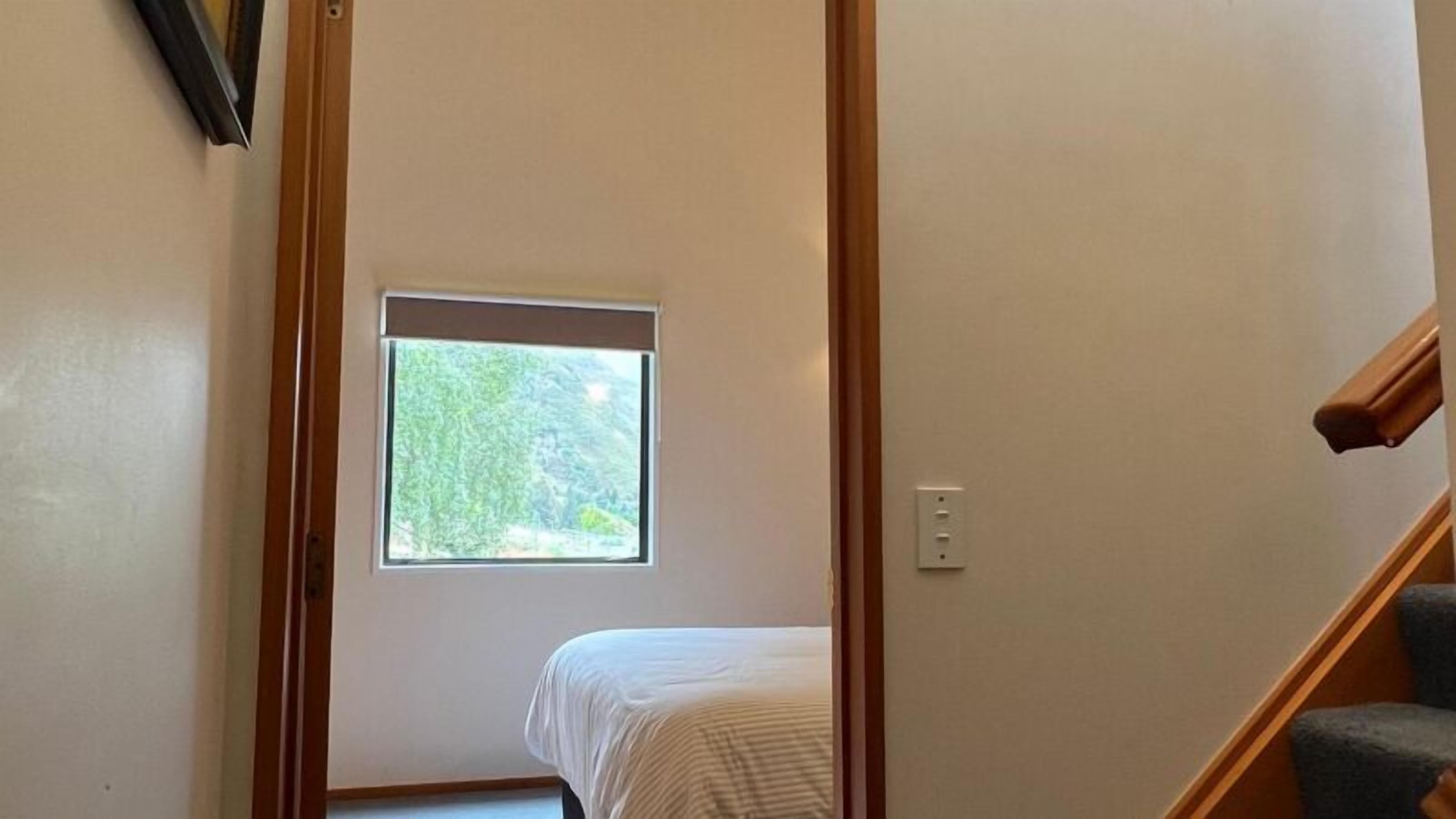 A narrow hallway with a small window, a bed, and a staircase.