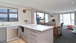 Una cocina moderna con una isla central, un comedor con mesa de madera y amplias ventanas que ofrecen luz natural.
