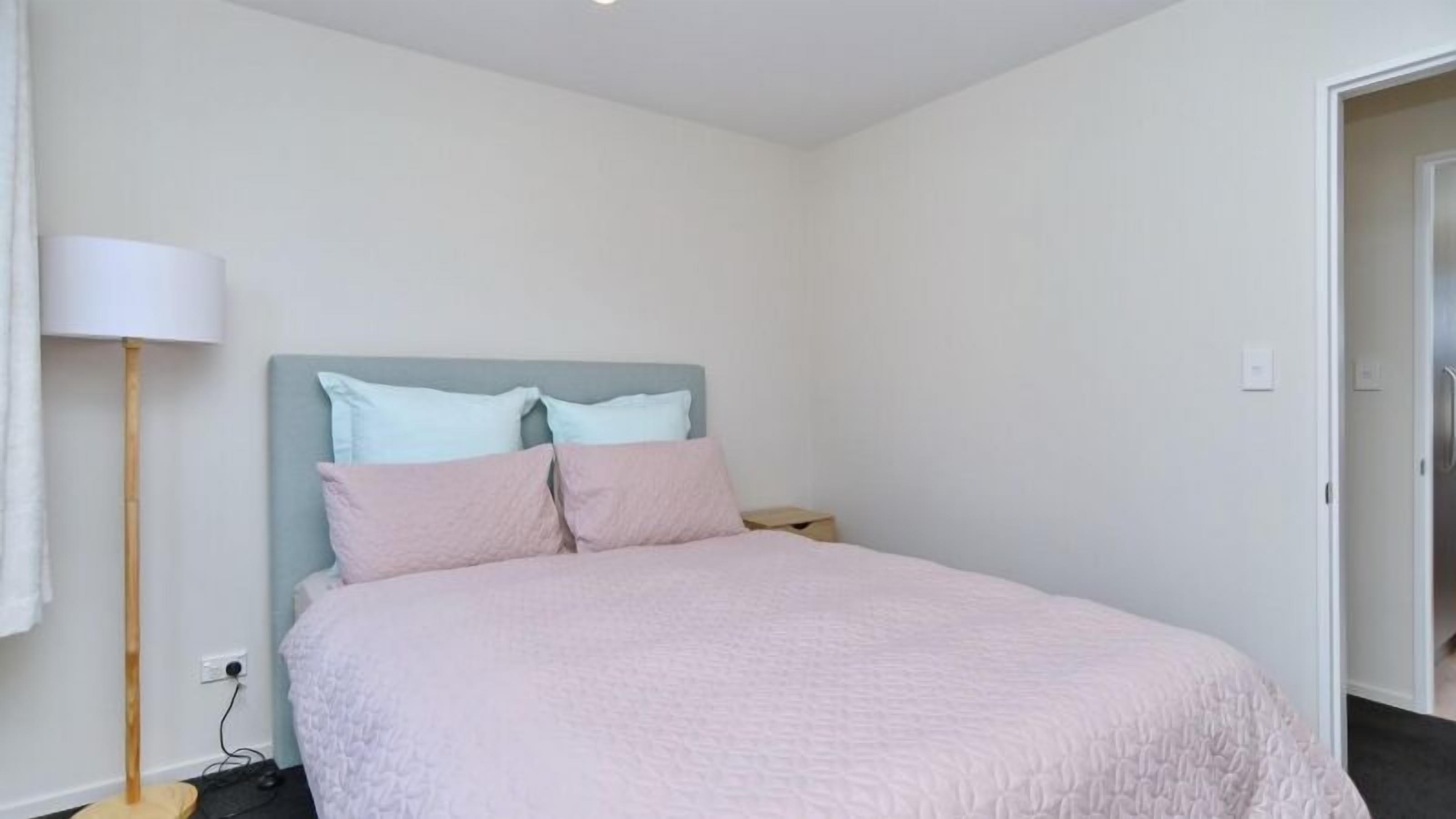 Ein Schlafzimmer mit Bett, Nachttisch, Lampe und Tür.