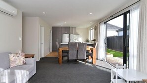 Una sala moderna con un sofá, una mesa de comedor con sillas y una zona de cocina al fondo.