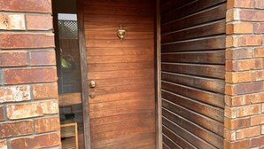 A wooden door with a brass handle, flanked by brick walls and a wooden slatted door on the right.
