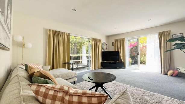 A living room with a sofa, a coffee table, a TV, and a sliding glass door leading to a garden.