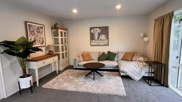 Una sala de estar con sofá, una mesita de centro y un aparador. Hay una planta, un cuadro y una lámpara.