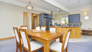Un comedor moderno con una mesa y sillas de madera, una cocina al fondo y vistas al exterior.