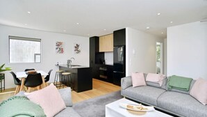 A modern living room with a grey sofa, a dining table with chairs, and a kitchen area with black appliances. - Worcester Terrace 201 - Luxurious City Apartment (Christchurch)