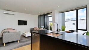 A modern kitchen with a black countertop and a built-in sink, a grey sofa with cushions, and a large window offering a city view. - Worcester Terrace 201 - Luxurious City Apartment (Christchurch)