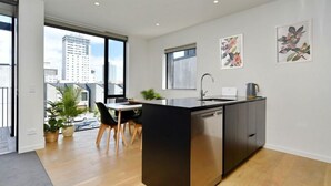 A modern kitchen with a central island, a dining area with chairs, and a view of the city through large windows. - Worcester Terrace 201 - Luxurious City Apartment (Christchurch)