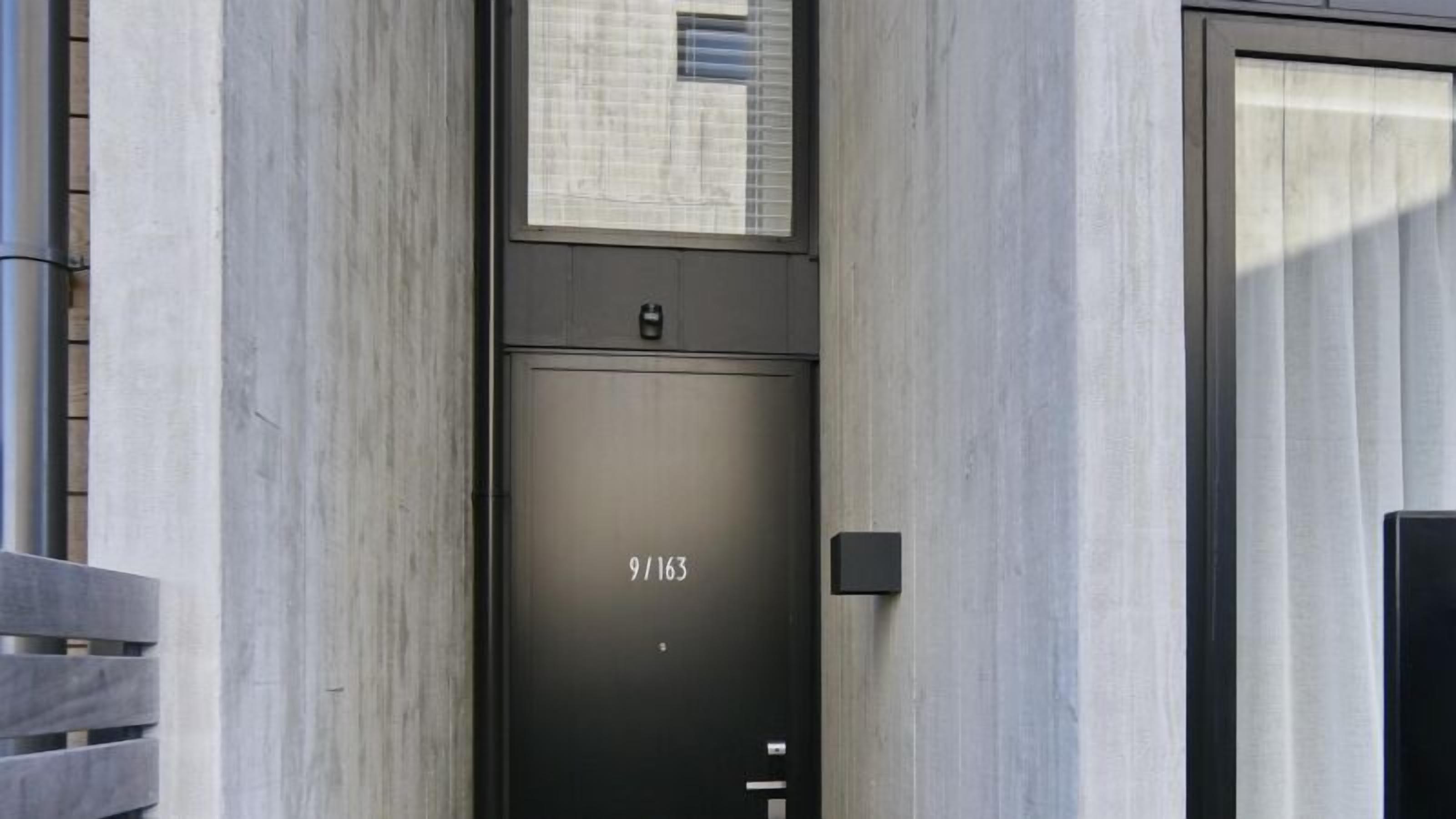 Une entrée moderne d’un immeuble, avec une porte en métal portant l’inscription « 9/163 ».