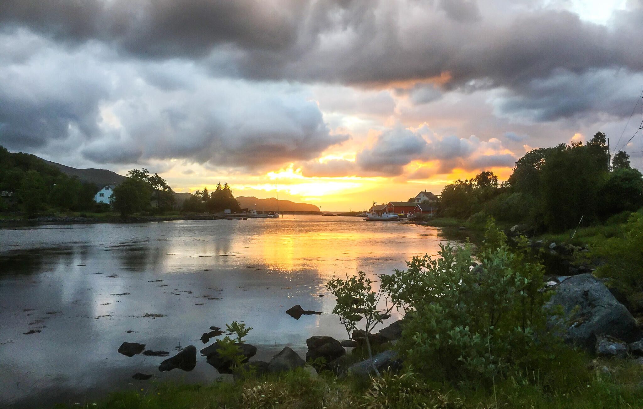 Un río con barcos, rodeado de vegetación y casas, al atardecer.