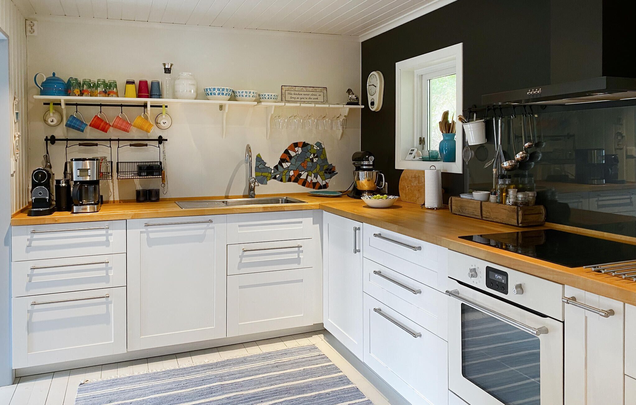 A modern kitchen with white cabinetry, a wooden countertop, a coffee maker, a kettle, and a clock on the wall.