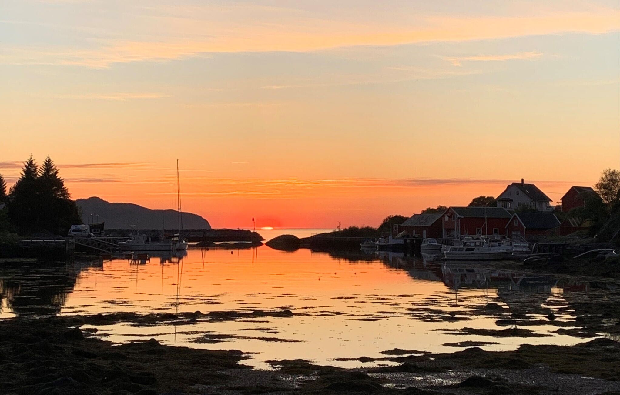 A sunset over a calm river with boats, a dock, and houses along the shore.