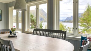 Un comedor con una gran mesa, sillas y vista a un lago y montañas.